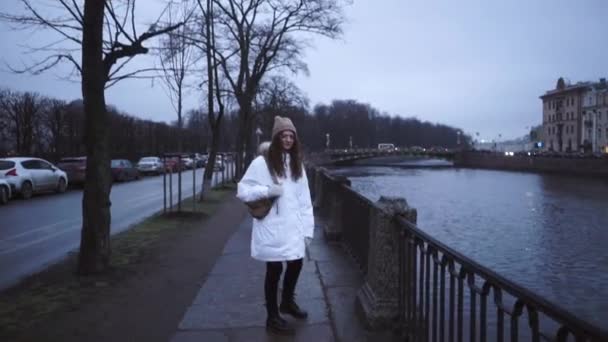 Beyaz ceketli bir kız caddede yürüyor. Moika nehrinin kıyısında genç bir kadın. Bulutlu Saint Petersburg. - Video, Çekim