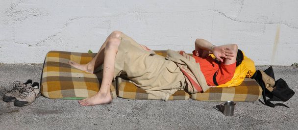 homeless man sleeps on a filthy mattress on the ground in the street above the sidewalk - Photo, Image