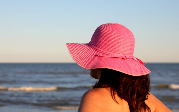 jonge vrouw met paarse hoed tijdens het zonnebaden op het strand aan de zee - Foto, afbeelding