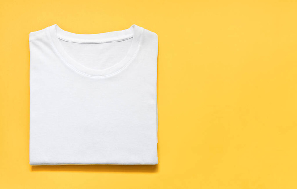 黄色の背景に折り畳まれた白い色のTシャツのトップビュー、コピースペース、フラットレイ - 写真・画像
