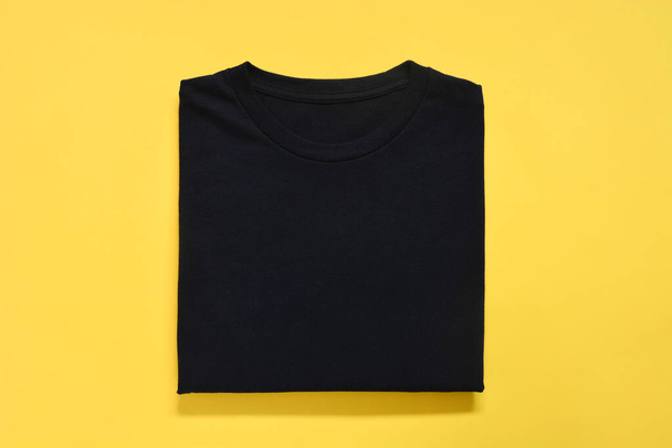 top view of folded black color t-shirt on yellow background, copy space, flat lay - Zdjęcie, obraz