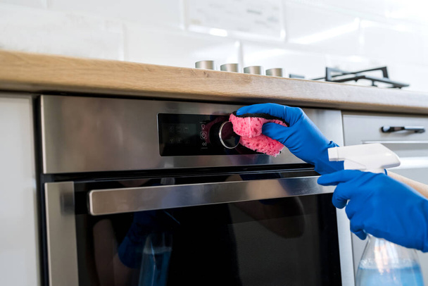 mujer joven limpiando el horno con guantes de goma y trapo. concepto de limpieza - Foto, Imagen