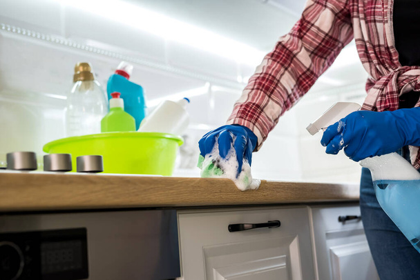 joven mujer limpieza en guantes de goma y esponja en la cocina en casa
. - Foto, Imagen