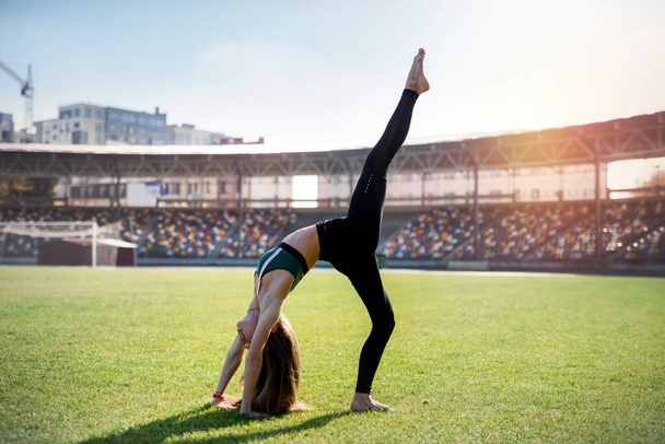 красива жінка спортсменка розтягує своє тіло на траві стадіону
. - Фото, зображення