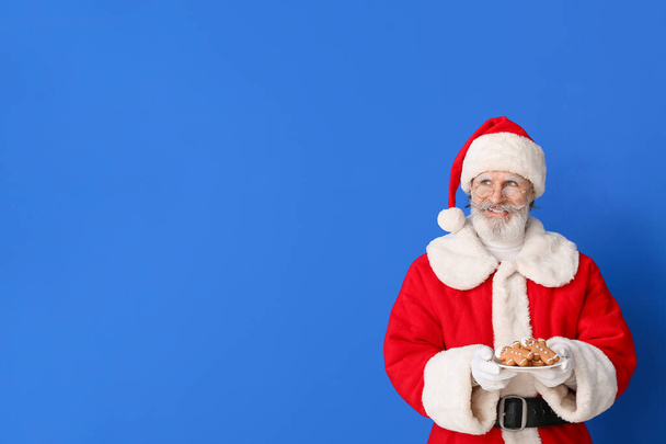 Santa Claus with tasty gingerbread cookies on color background - Photo, Image