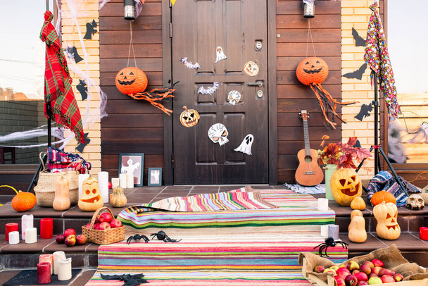 Door of country house decorated with halloween symbols in front of staircase with jack-o-lanterns, spiders, bats, apples and candles - Фото, изображение