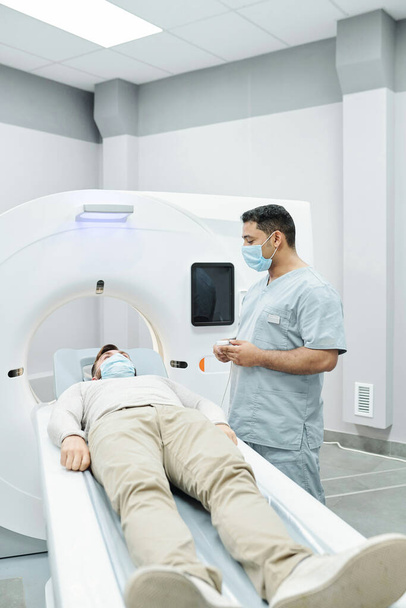 Lekarz i pielęgniarka w maskach chirurgicznych analizujących obraz rentgenowski podczas snu pacjenta w pokoju szpitalnym - Zdjęcie, obraz