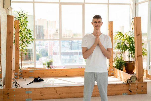 Happy young sportsman in activewear making namaste gesture while standing in front of camera against equipment for aerial yoga training - Photo, Image