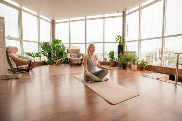 Young serene female crossing legs while sitting on mat in pose of lotus and practicing meditation exercise on the floor in home environment - Photo, Image