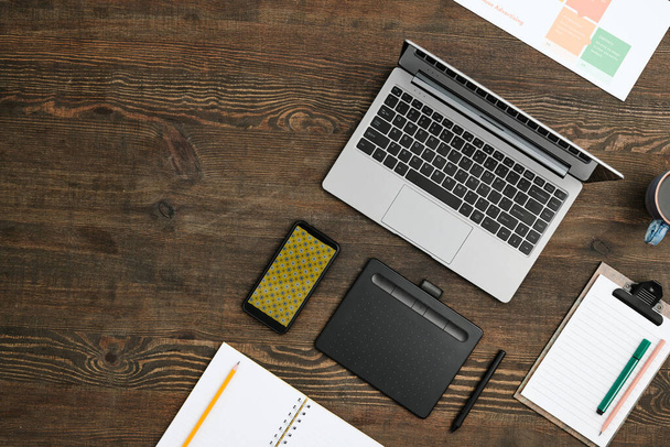 плоская компоновка мобильных гаджетов, напиток, открытый ноутбук с карандашом и буфером обмена с рабочим документом и маркером на деревянном столе - Фото, изображение