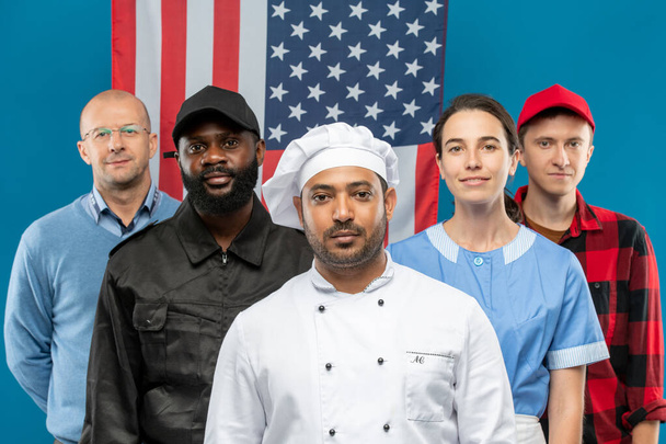 electorado contemporáneo de diversas etnias, culturas, géneros y ocupaciones en su uniforme de pie contra la bandera estadounidense - Foto, imagen