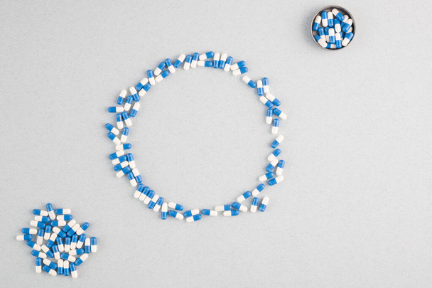 Flat layout of large circle over white background made up of blue-and-white medical capsules with the same pills near by in isolation - Photo, Image