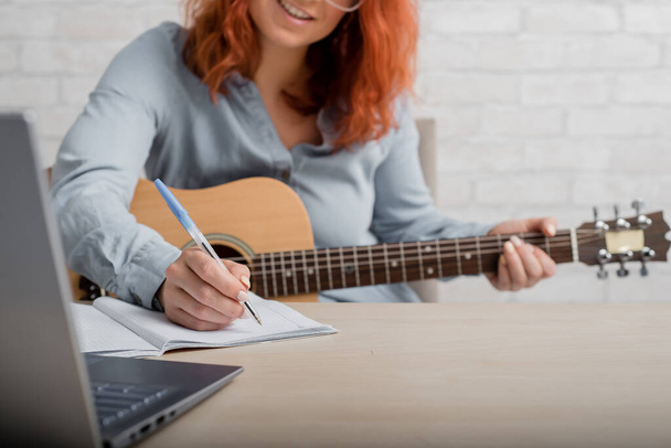 Una mujer con una guitarra escribe notas en un cuaderno. La chica compone una canción - Foto, imagen