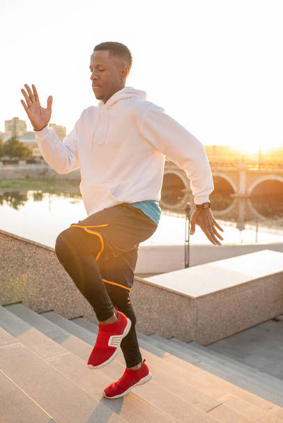 Jonge extatische sportman van Afrikaanse etniciteit springen over de bovenste trap van marmeren trap tijdens het sporten in de stedelijke omgeving - Foto, afbeelding