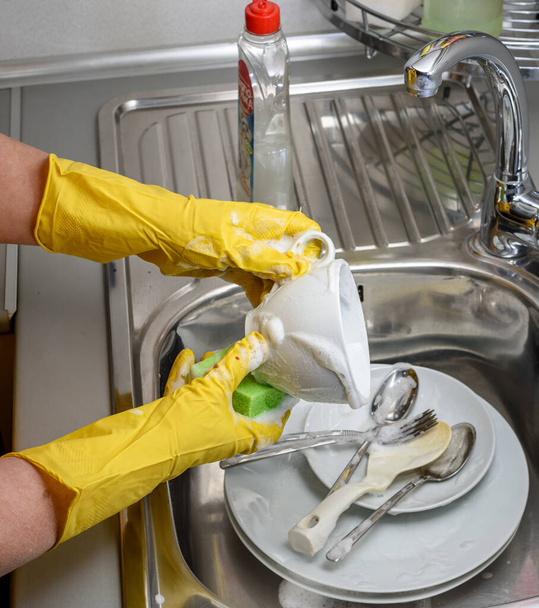 A woman in rubber gloves washes dishes in the kitchen sink, hands only - Foto, Imagen