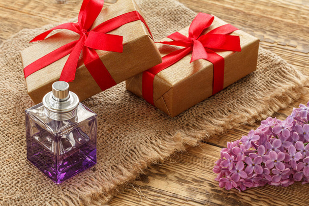 Egy üveg parfüm, ajándékdobozok és orgonavirág a zsákvásznon és a fa deszkákon. Fogalom az ajándékozásról az ünnepekkor. Felülnézet. - Fotó, kép