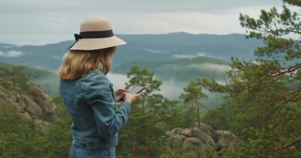 Uma mulher está em pé no topo de um penhasco e enviando uma mensagem em seu smartphone. 4K DCI - Filmagem, Vídeo