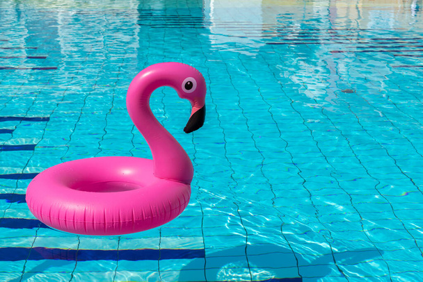 Vaaleanpunainen allas. Vaaleanpunainen puhallettava flamingo uima-altaassa veden kesärannalla tausta. Allasbileet - Valokuva, kuva
