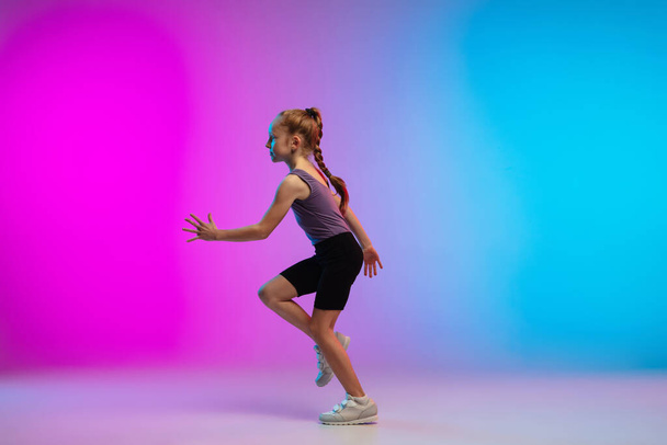 Teenage girl running, jogging against gradient pink-blue neon studio background in motion - Foto, Bild