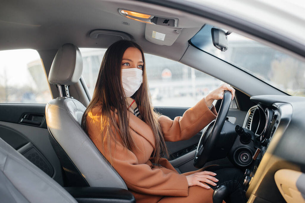 A young girl sits behind the wheel in the car in the mask during the global pandemic and coronavirus. Quarantine - Foto, Imagem