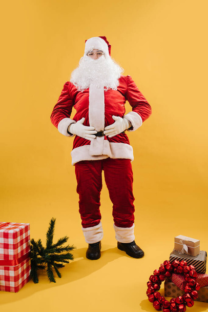 サンタクロースは黄色の背景の上に彼の胃にしがみついて笑う - 写真・画像