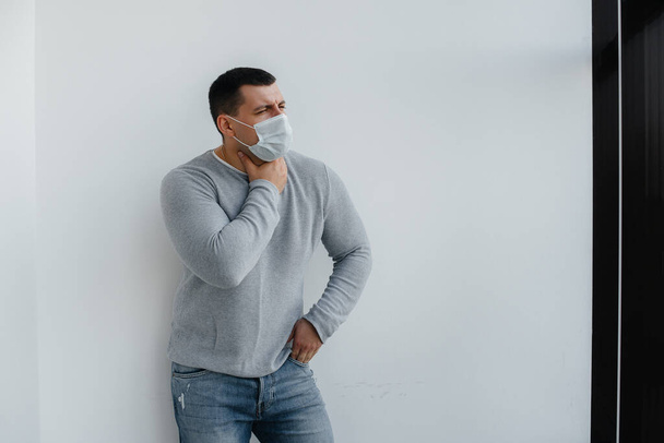 A young man stands on a gray background wearing a mask during a quarantine with free space. Quarantine in the mask - Foto, Imagen