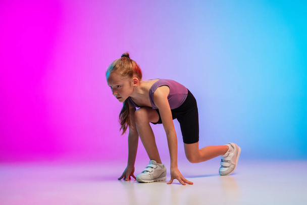 Teenage girl running, jogging against gradient pink-blue neon studio background in motion - Фото, зображення