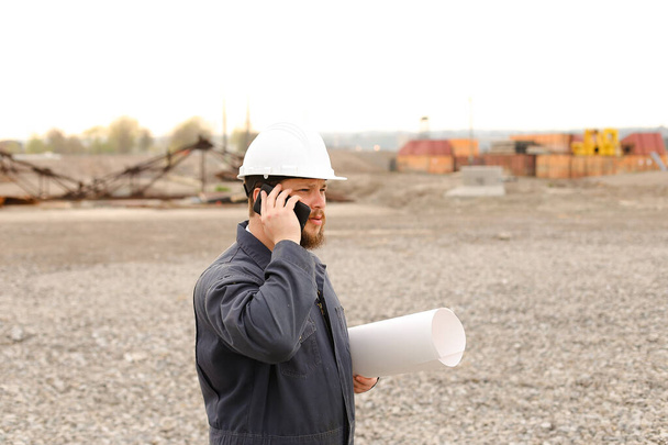 Beyaz ustabaşı, VHF telsizinden ve inşaat alanındaki kağıtlardan konuşuyor.. - Fotoğraf, Görsel