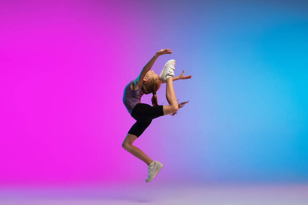 Teenage girl running, jogging against gradient pink-blue neon studio background in motion - Fotó, kép