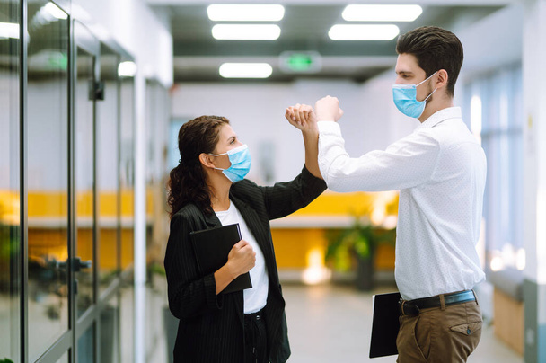 Two manager in protective medical masks bumping elbows while greeting each other in in modern office. Business partners handshake during coronavirus. Covid-19. - Photo, image