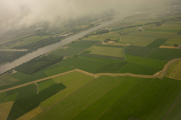 Farmy v Holandsku, Nizozemsko s průplavem pozorovaným z letadla na obloze s mraky z okna v letadle - Fotografie, Obrázek