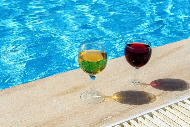 Two glasses of red and white wine are placed by the pool. The concept of a pleasant stay - Foto, Imagem