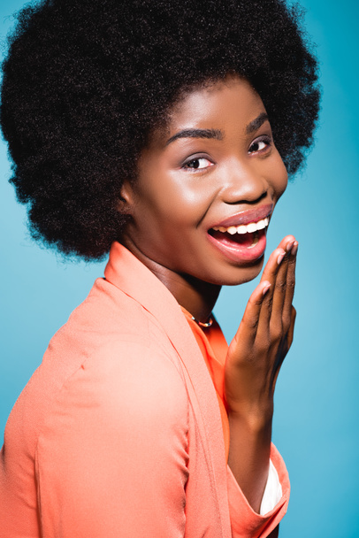 feliz afroamericana joven mujer en naranja elegante traje aislado sobre fondo azul - Foto, imagen