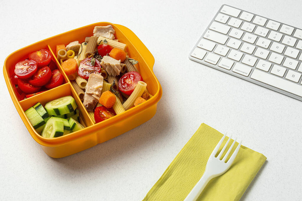 Lunch at work place healthy pasta with tuna, cherry tomatoes, carrot, cucumber in lunch box on work table. Home food for office concept - 写真・画像