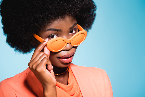 african american young woman in orange stylish outfit isolated on blue background - Foto, Imagem