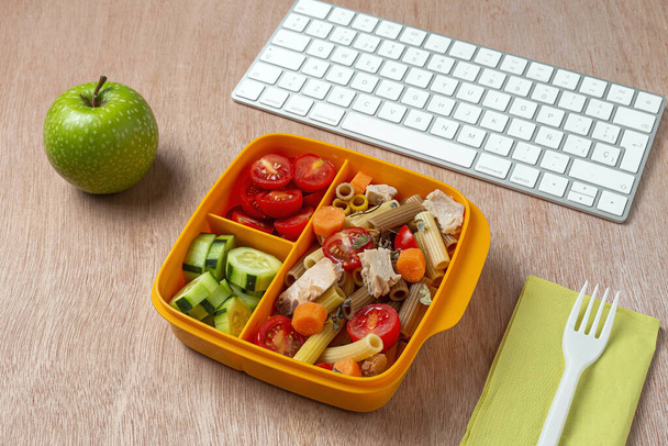 Lunch at work place healthy pasta with tuna, cherry tomatoes, carrot, cucumber in lunch box on work table. Home food for office concept - Foto, afbeelding