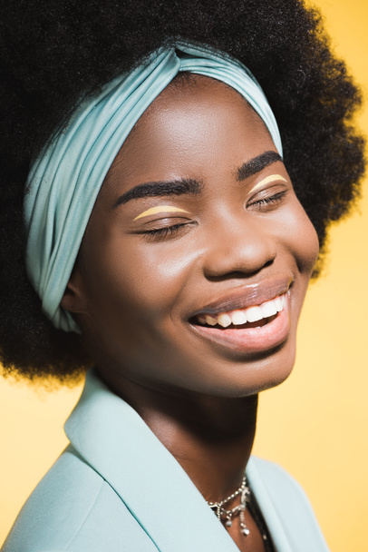 riéndose africana americana joven mujer en azul elegante traje aislado en amarillo  - Foto, imagen