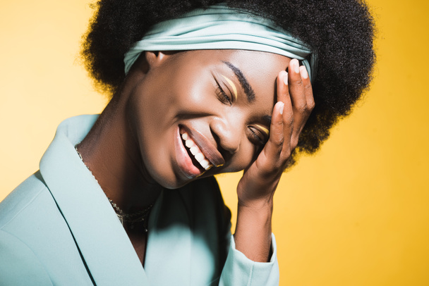 laughing african american young woman in blue stylish outfit isolated on yellow  - Фото, изображение