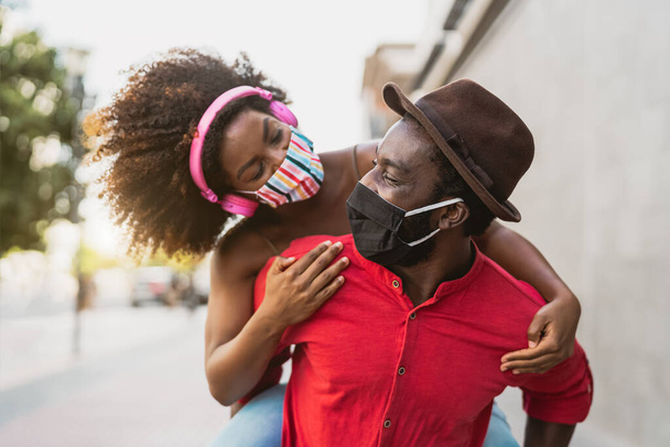 Africano casal piggyback usando máscara facial - Happy Afro pessoas se divertindo ao ar livre - Cuidados de saúde e conceito de relacionamento de jovens - Foto, Imagem