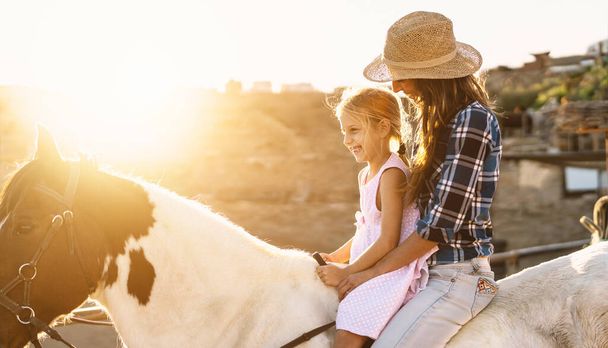 Happy family mother and daughter having fun riding horse inside ranch - Photo, Image