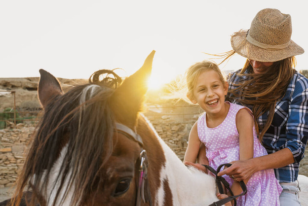 Família feliz mãe e filha se divertindo montando cavalo dentro do rancho - Foto, Imagem