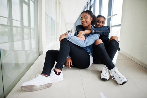 Two african woman friends in jeans jacket sitting indoor together. - Foto, Imagen