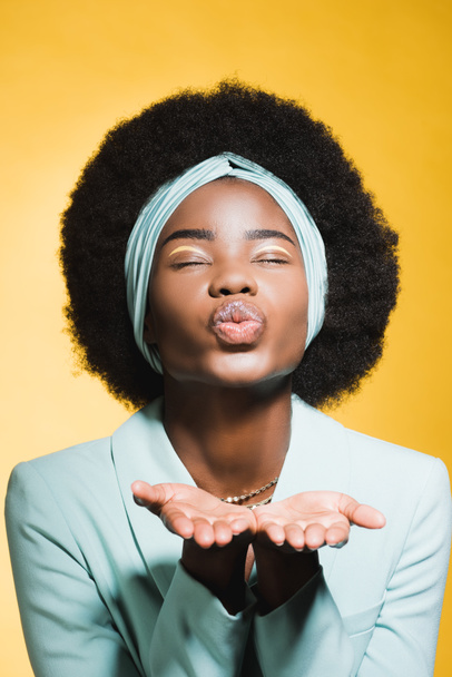 african american young woman in blue stylish outfit blowing kiss isolated on yellow  - Foto, Imagem
