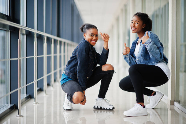 Two african woman friends in jeans jacket show thumb up indoor together. - Fotoğraf, Görsel