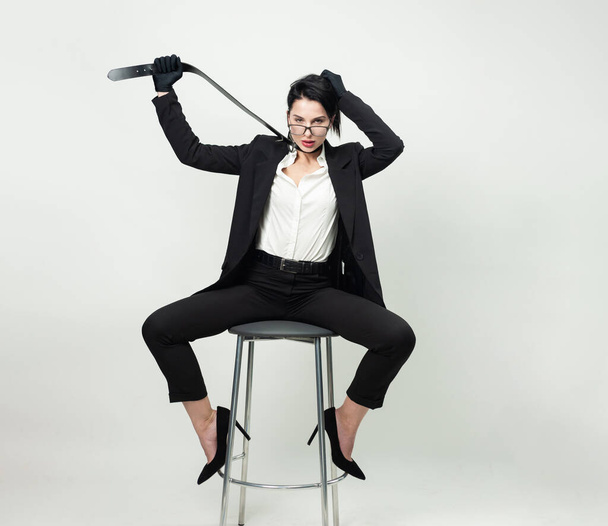 een vrouw in zwarte kantoorkleding en handschoenen zit op een stoel met een riem om haar nek - Foto, afbeelding