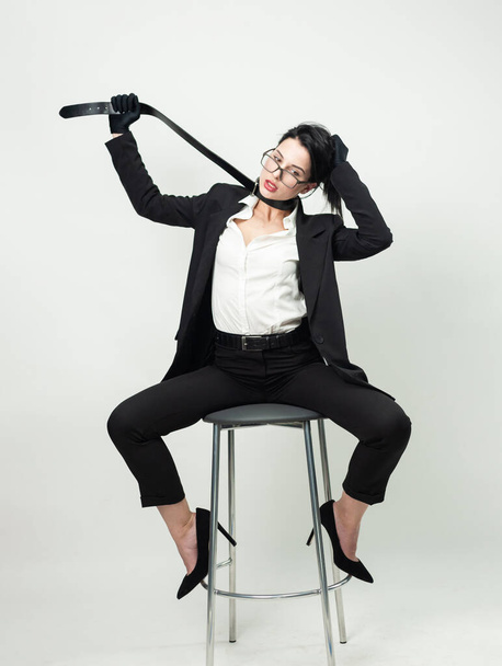 uma mulher de escritório preto roupas e luvas está sentado em uma cadeira com um cinto em torno de seu pescoço - Foto, Imagem