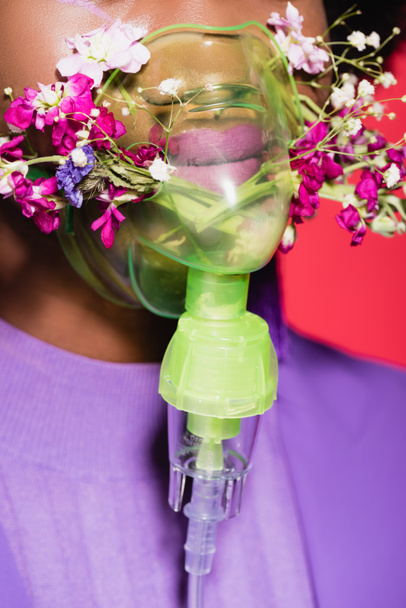 cropped view of african american young woman in purple stylish outfit with flowers in inhaler isolated on red - Foto, afbeelding