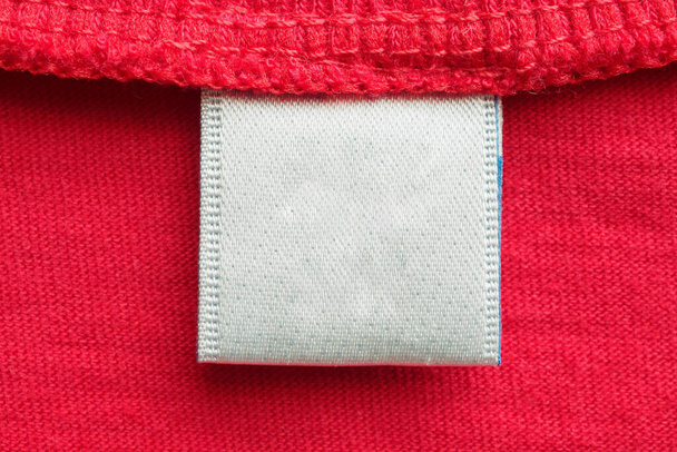 Белая пустая прачечная этикетка ухода за одеждой на фоне красной хлопковой рубашки - Фото, изображение