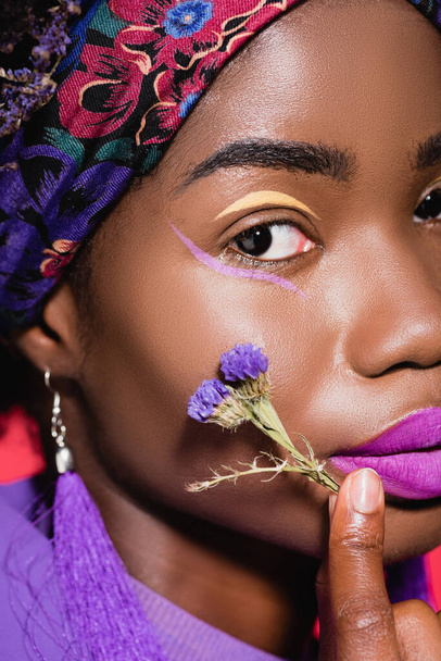 closeup of african american young woman with purple flower isolated on red - Fotografie, Obrázek