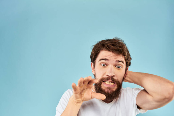Hombre emocional con una barba en una camiseta blanca fondo azul estilo de vida divertido - Foto, imagen